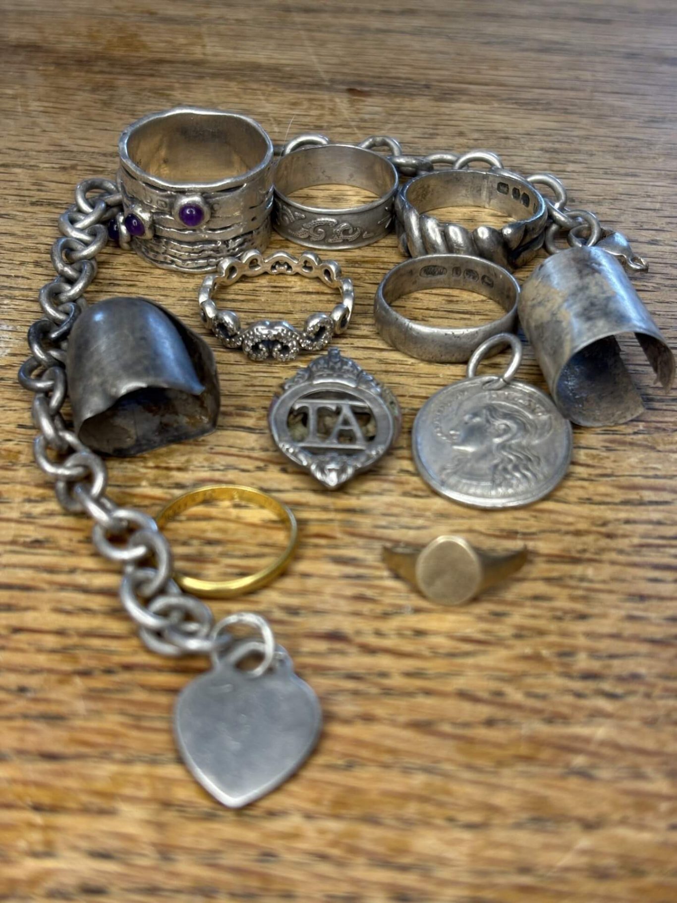 A collection of assorted silver rings and a charm bracelet on a wooden surface.