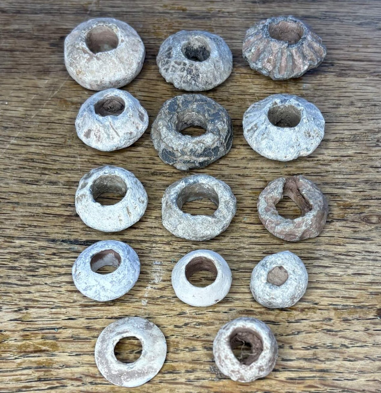 A collection of various shaped lead spindle whorls arranged on a wooden surface.