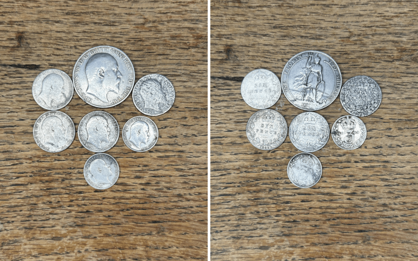 A collection of Edward 7th silver coins displayed on a wooden surface.