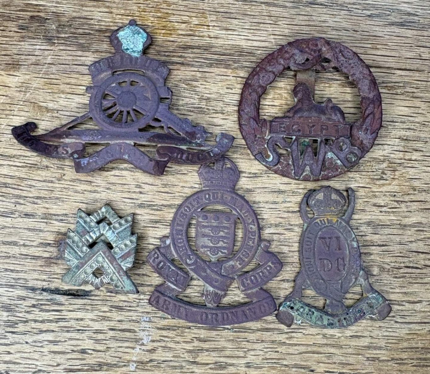 Five antique military badges, featuring intricate designs, displayed on a wooden surface.