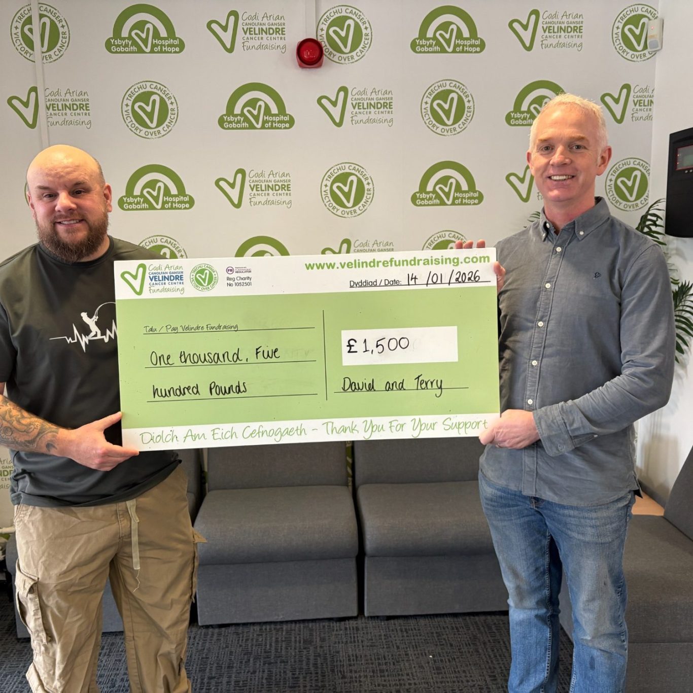 Dave and Terry hold a large cheque for €1,500 in a bright office setting.