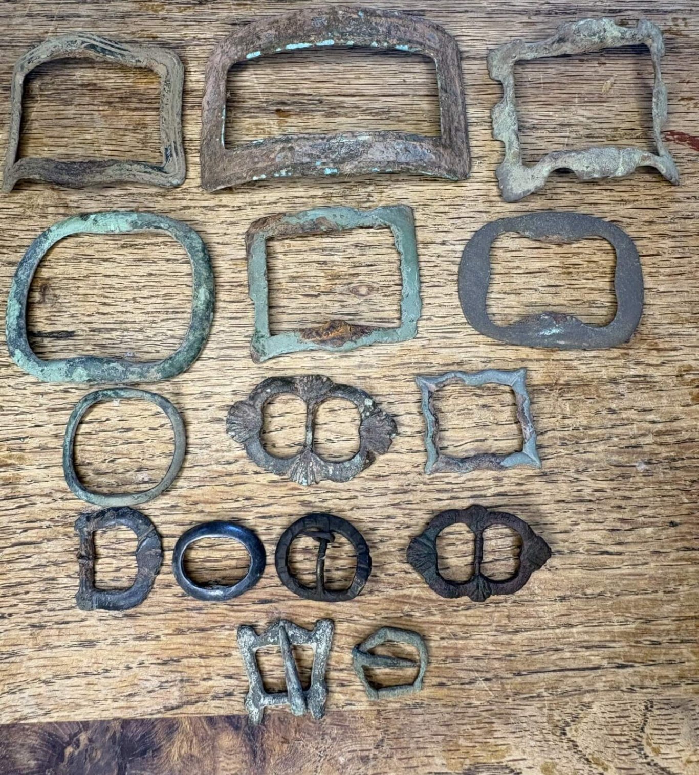 Collection of various old metal buckles and frames on a wooden surface.